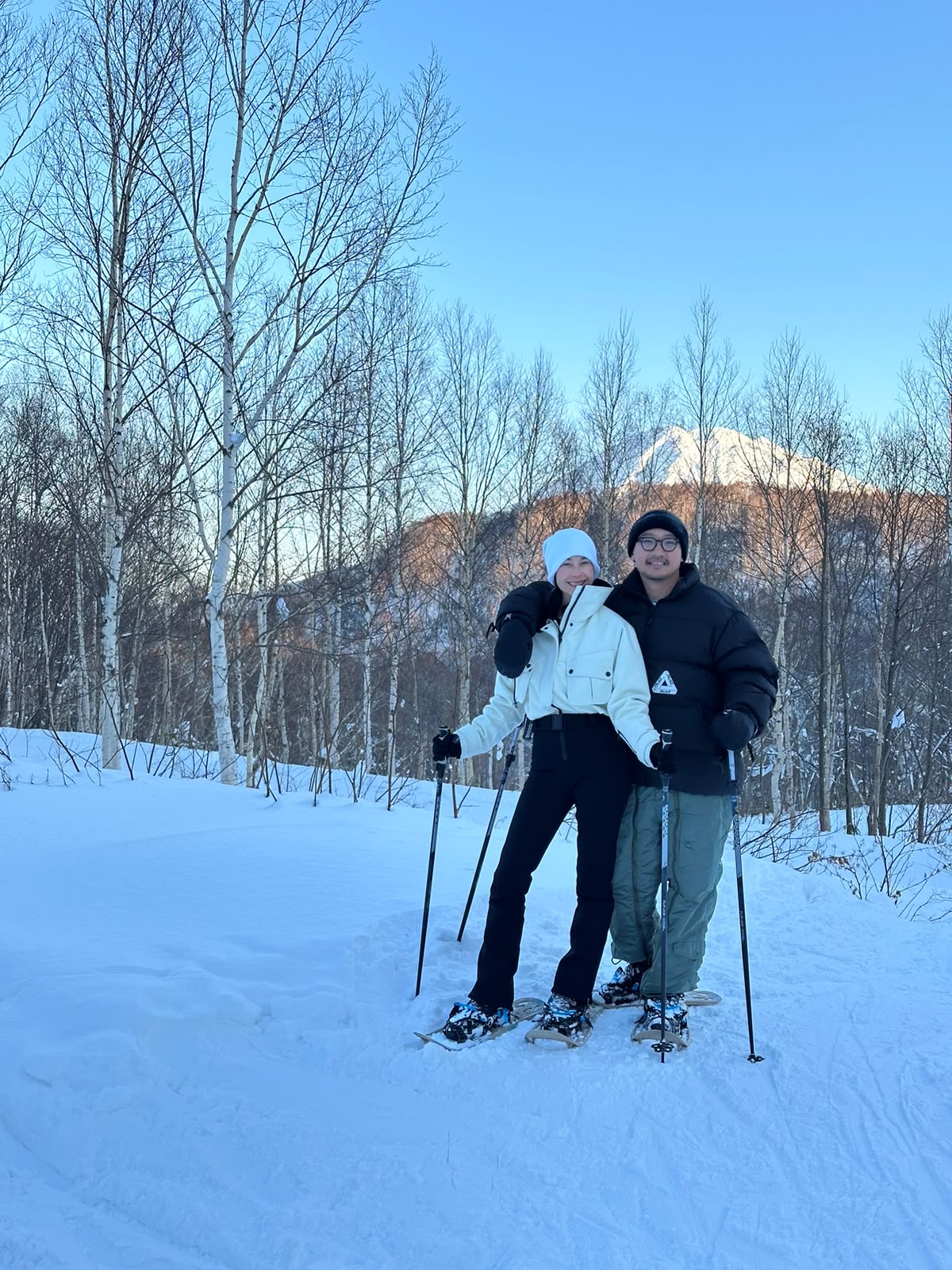 Two guests snowshoeing among birch trees with Mount Yotei behind them